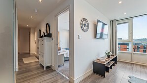 Ein modernes Hotelzimmer mit Holzboden, einem Bett, einem Schreibtisch mit Computer, einem Fernseher und einem großen Fenster mit Blick auf die Stadt.