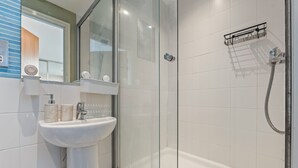 Ein Badezimmer mit einer Duschkabine, einem weißen Waschbecken und einem Spiegel.