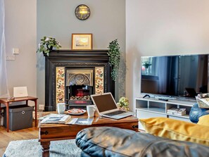 Ein Wohnzimmer mit Kamin, Fernseher, einem Laptop auf einem Holztisch und einer Couch.