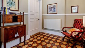 A room with a checkered floor, a red leather chair, a white door, and framed artwork on the walls. - 1 Bed in Penmaenmawr (oc-95495) (Penmaenmawr)