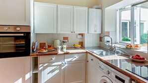 A modern kitchen with white cabinets, a built-in oven, a washing machine, and a large window providing natural light. - 1 Bed in Penmaenmawr (oc-95495) (Penmaenmawr)