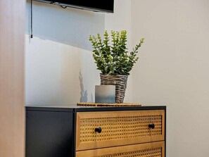 A flat-screen TV mounted on a wall, a woven basket with a plant on top of a cabinet, and a wooden cabinet with drawers. - 1 Bed in Newport (oc-95453) (Newport)