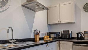 Een moderne keuken met een roestvrijstalen spoelbak, een magnetron, een koffiezetapparaat en witte kastjes.