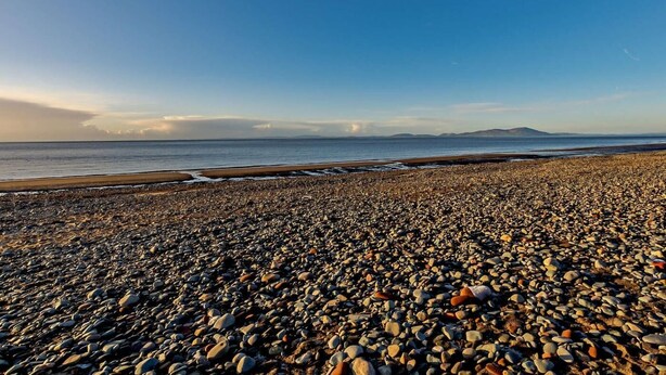 Ein Kiesstrand mit blauem Himmel und Bergen in der Ferne.