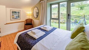 Ein Schlafzimmer mit Bett, Sessel, Lampe, einem Gemälde und Blick ins Freie.