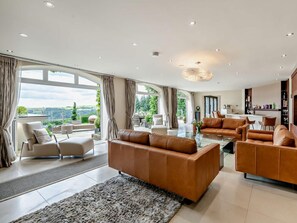 Ein geräumiges Wohnzimmer mit Ledersofas, einem Glastisch und großen Fenstern mit Blick ins Freie.