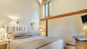 Un dormitorio con cama, lámparas de noche, televisión, escritorio de madera y ventana.