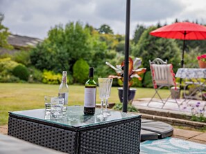 An outdoor seating area with a glass-top table, two bottles of wine, and two glasses. - 2 Bed in Hemel Hempstead (oc-95536) (Great Gaddesden)