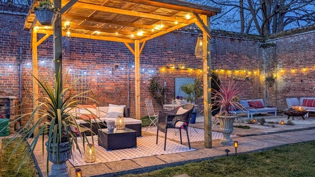 Ein überdachter Patio-Bereich mit Sitzgelegenheiten, Lichterketten und Topfpflanzen.