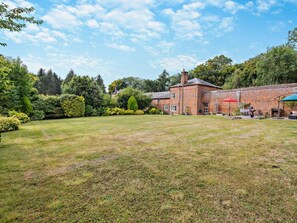 A spacious backyard with a brick building, a lawn, and a variety of trees and shrubs. - 2 Bed in Hemel Hempstead (oc-95536) (Great Gaddesden)