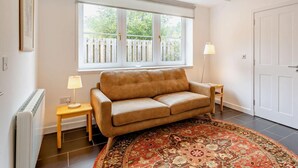 Ein Wohnzimmer mit einer Couch, einem gemusterten Teppich, einem Fenster mit Blick auf einen Zaun und einer Tür.
