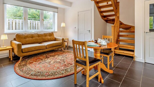 Ein Wohnzimmer mit einer Couch, einem runden Tisch mit Stühlen, einem gemusterten Teppich und einer Holztreppe.