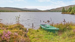 Ein ruhiger See mit einem grünen Boot, das an der Ufer angelegt ist, umgeben von grünen Wiesen und Hügeln im Hintergrund.