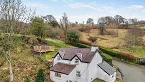A white house with a sloped roof, a wooden deck, and a stone wall. - 2 Bed in Corwen (oc-95542) (Corwen)