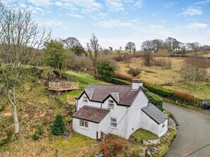 A white house with a sloped roof, a wooden deck, and a stone wall. - 2 Bed in Corwen (oc-95542) (Corwen)