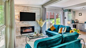 Ein modernes Wohnzimmer mit Kamin, einer Couch, einem Fernseher und Blick ins Freie.