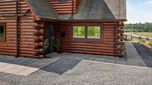 A log cabin with a sloped roof, a front porch, and a view of a lake. - 4 Bed in Kippford (oc-95234) (Kippford)