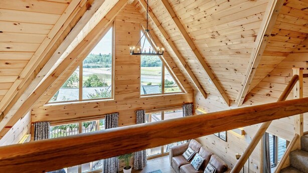 A high-ceilinged wooden interior with a large window offering a view of a lake and trees. - 4 Bed in Kippford (oc-95234) (Kippford)