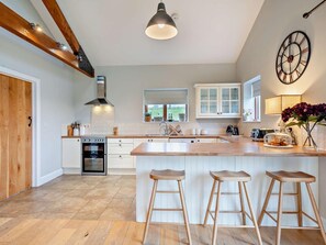 Eine Küche mit einer zentralen Kochinsel, Holzstühlen, einem eingebauten Ofen und einer großen Wanduhr.