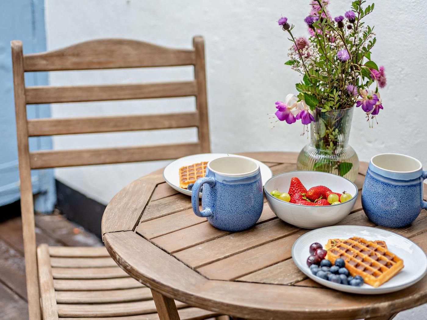 Una mesa de madera con un gofre, un bol de fruta y dos tazas.