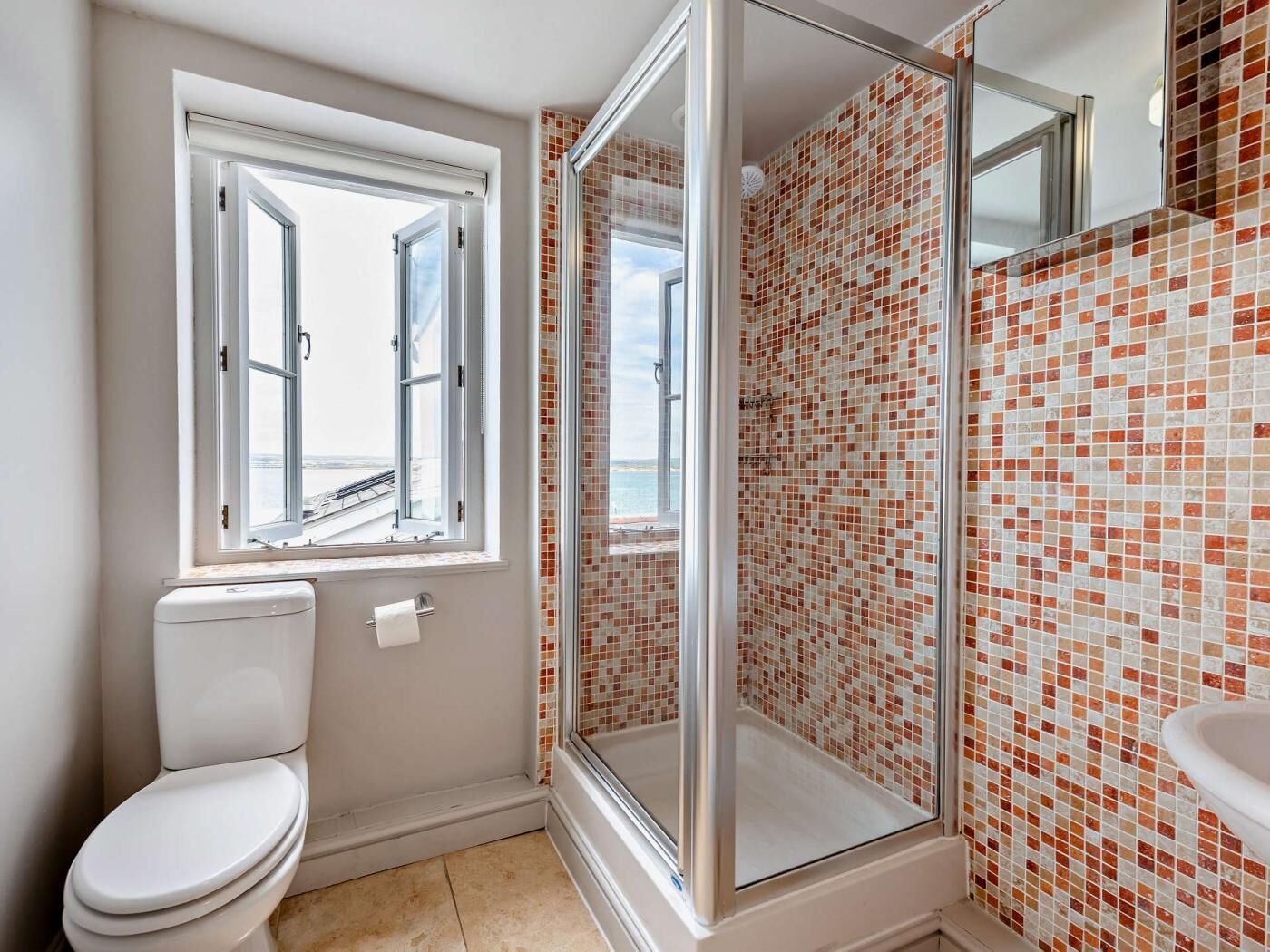 Ein Badezimmer mit Toilette, einer Dusche mit Glastür, einem Fenster und einer gefliesten Wand.