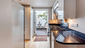 Eine moderne Küche mit schwarzem Arbeitsplatz, Edelstahlgeräten und Blick auf einen Balkon mit Gartenmöbeln.