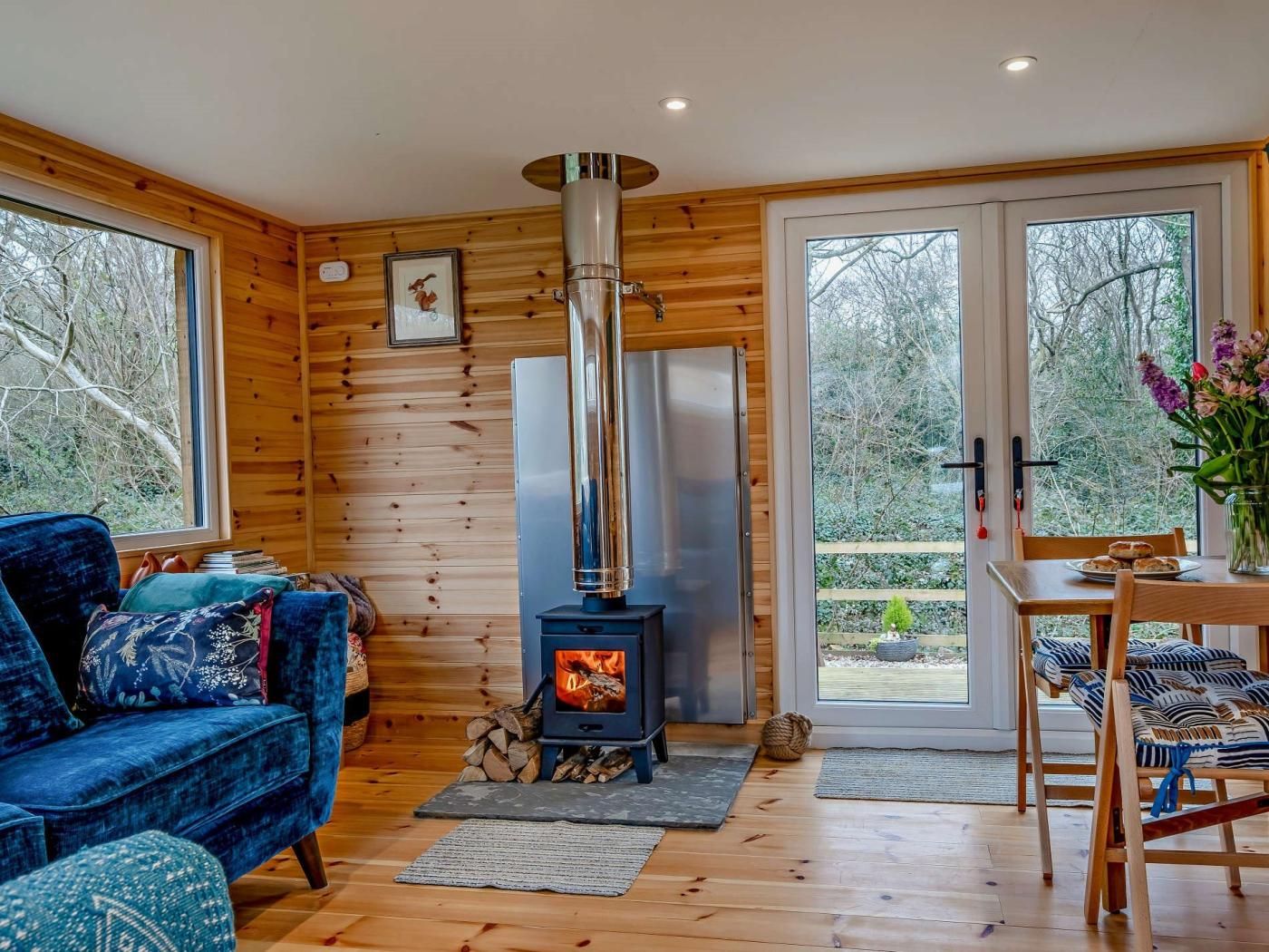 L’intérieur chaleureux d’un chalet avec un poêle à bois, un canapé bleu et une table à manger avec des chaises.
