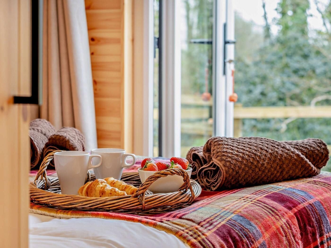 A cozy room with a bed, a wicker basket with croissants, a cup, and a bowl of strawberries.