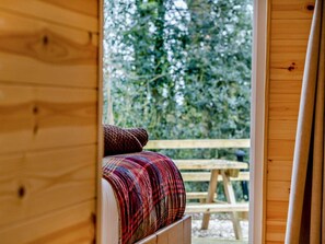 Ein Holzblock-Innenraum mit einem Bett und Blick auf eine Holzterrasse sowie dichtes Grün draußen.