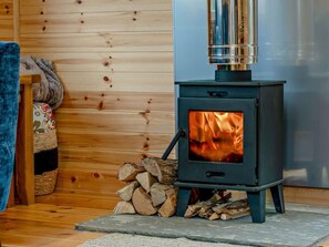 Ein Kaminofen mit Glastür, ein Holzstapel und eine Holzwand.