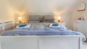 Ein Schlafzimmer mit einem weißen Bett, zwei Nachttischen inklusive Lampen, einem weißen Kleiderschrank und einem kleinen runden Spiegel an der Wand.