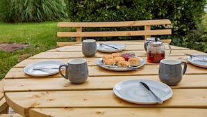 Ein draußen stehendes Holzpicknick-Set mit Tellern, Tassen und einem Teekrug.