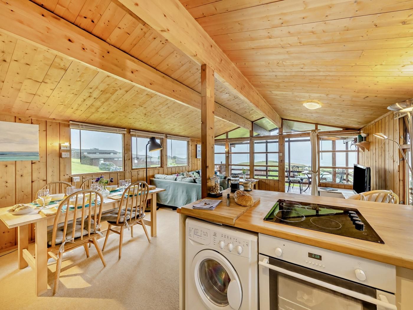 L’intérieur d’un chalet en bois comprend un coin repas, une cuisine et de grandes fenêtres offrant une vue panoramique.