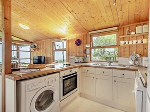 A compact kitchen with wooden walls, a built-in washing machine, a stove, and a sink.