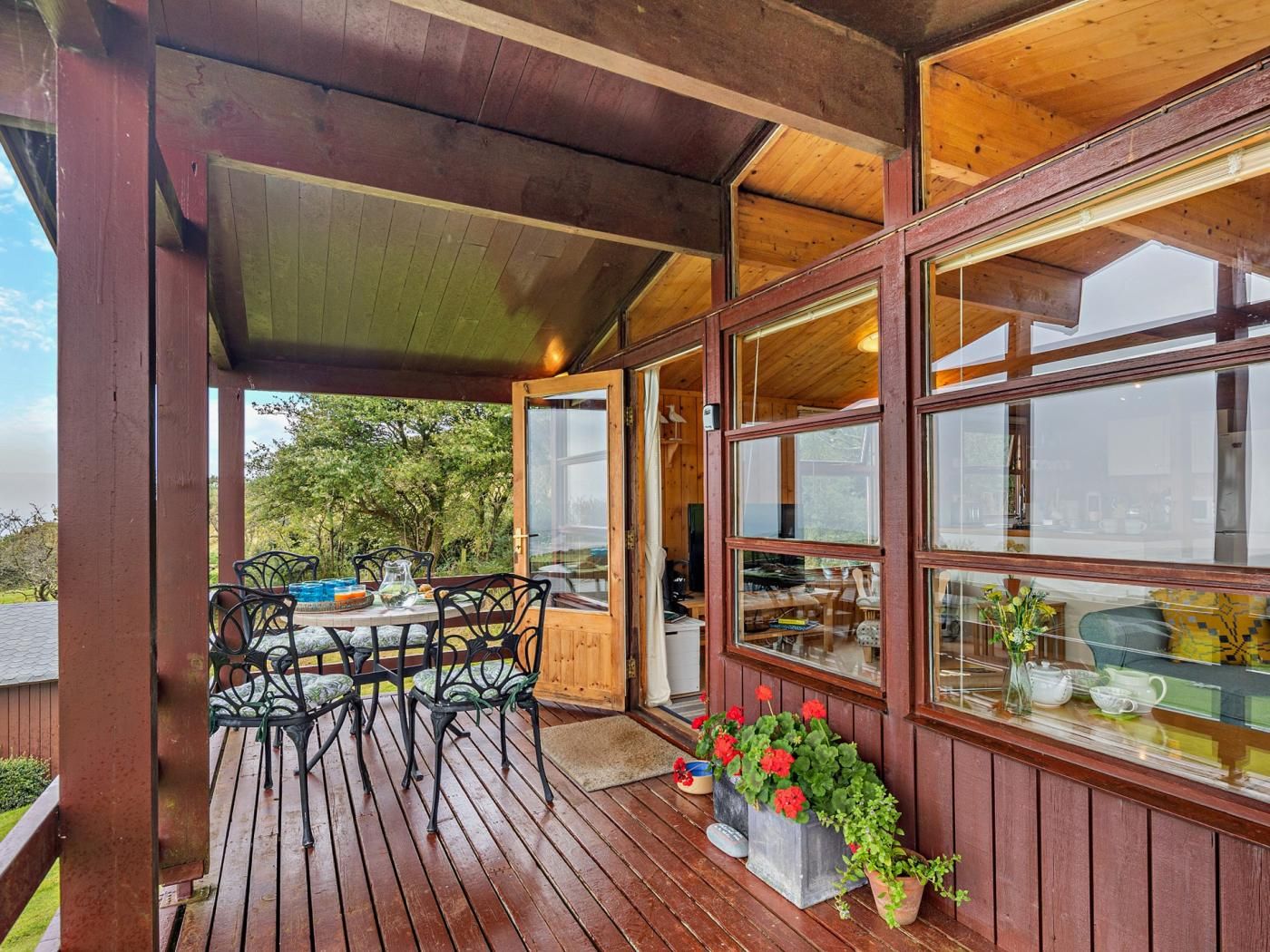 Une terrasse en bois avec une table et des chaises, de grandes fenêtres et des plantes en pot.
