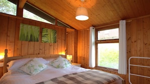 Quarto de cabana de madeira com uma cama, duas luminárias na parede e uma janela com cortinas.