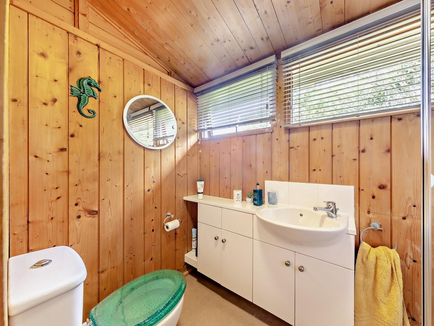 Une salle de bain rustique, aménagée dans une cabane en bois, avec des toilettes, une baignoire verte, un lavabo blanc et un miroir.