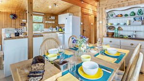 Interior de uma cabana de madeira com sala de jantar, cozinha e um relógio à vista.