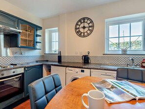 A kitchen with a dining area, a clock on the wall, and a window with a view. - 3 Bed in Workington (oc-92628) (Dean)