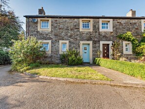 A stone house with a gravel driveway, a blue door, and a small garden. - 3 Bed in Workington (oc-92628) (Dean)