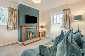 A living room with a fireplace, a television mounted above it, a sofa with cushions, and a lamp on a side table. - 3 Bed in Workington (oc-92628) (Dean)