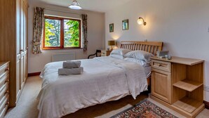 A bedroom with a bed, bedside tables, a nightstand, a window with curtains, a wall-mounted lamp, and a radiator. - 4 Bed in Kendal (oc-95607) (Crosthwaite)