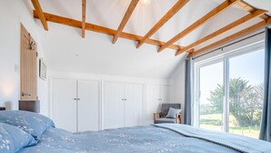 Un dormitorio con cama, armario, silla y ventana grande.