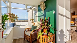 Una habitación con vista al mar, una silla de mimbre, una pared verde y una planta en maceta.