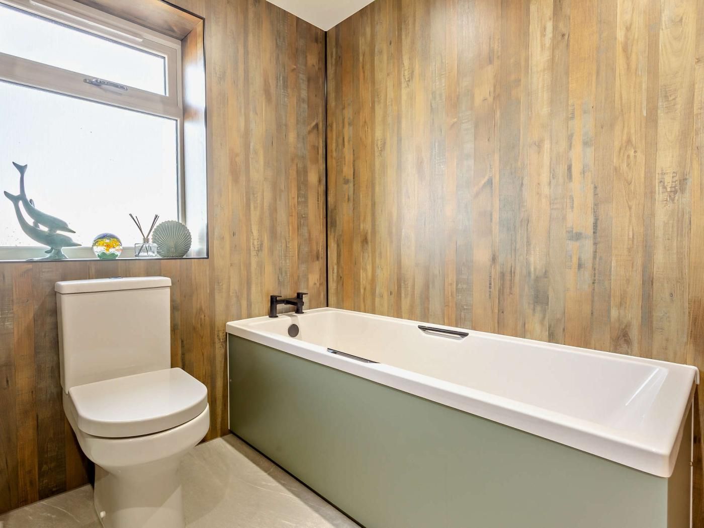 A bathroom with a white toilet, a bathtub, and wooden walls.
