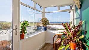 Una habitación con ventanas amplias, vista al mar y plantas en macetas.