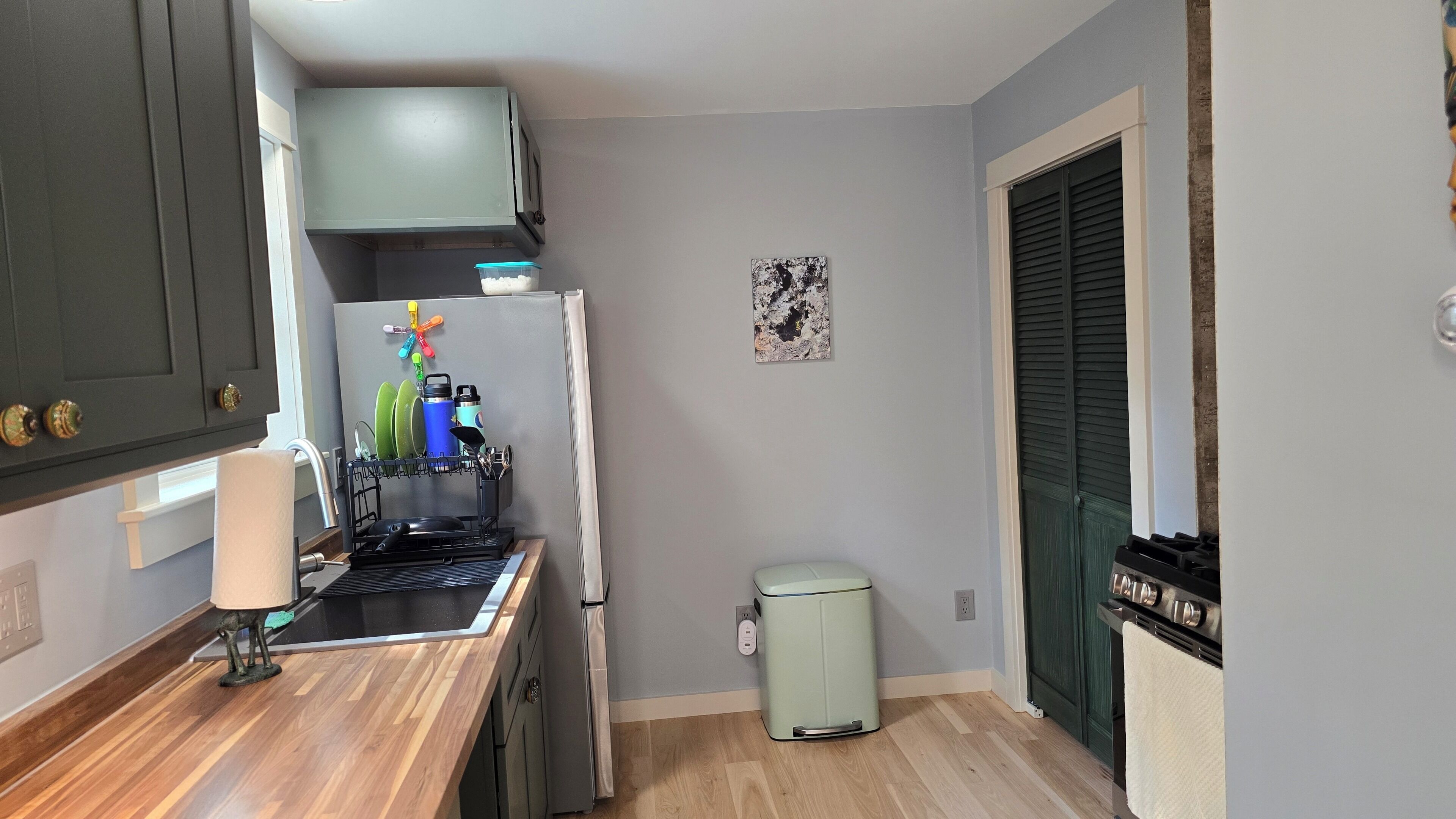 Cocina compacta con lavavajillas incorporado, un pequeño cubo de basura y un refrigerador.