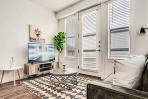 Ein Wohnzimmer mit Fernseher, rundem Couchtisch, Sofa und einer Pflanze.