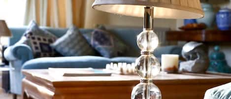 En tydlig bild av en lampa med en veckad lampskärm, ett träbord och en blå soffa med mönstrade kuddar.