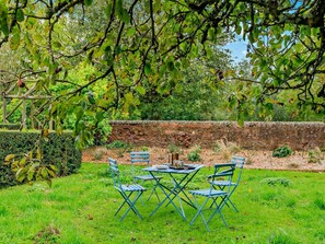 Un jardí amb una taula i caires, una paret de pedra i diferents plantes.
